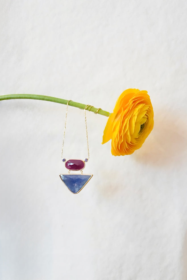 Necklace with purple and blue pendant next to a yellow flower on a white background