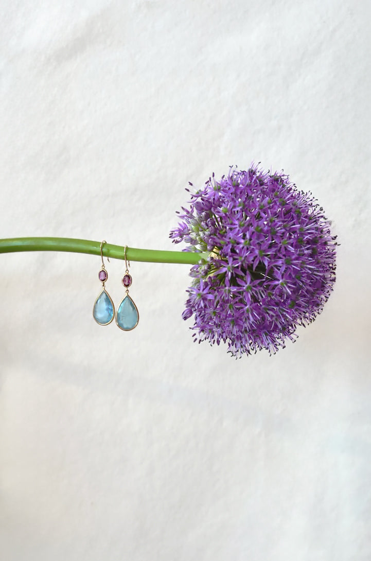 Purple flower with two teardrop-shaped aquamarine earrings on a white background