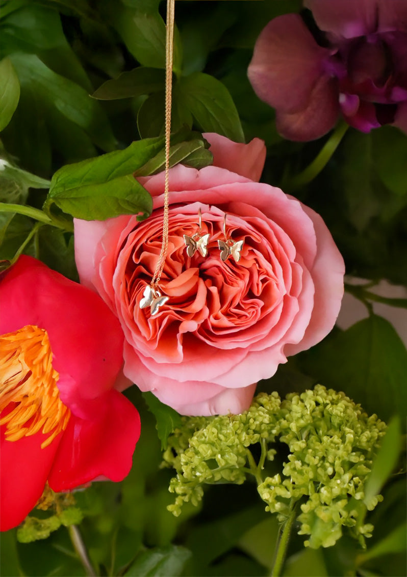 Pink rose with gold butterfly charm surrounded by green leaves and flowers