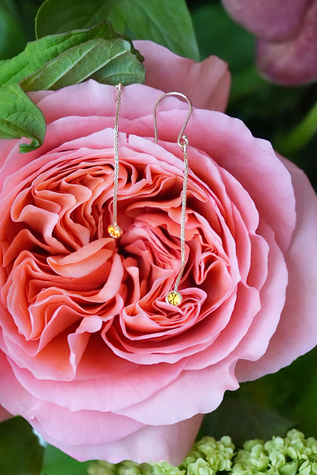 Gold earrings with small yellow stones on a pink rose