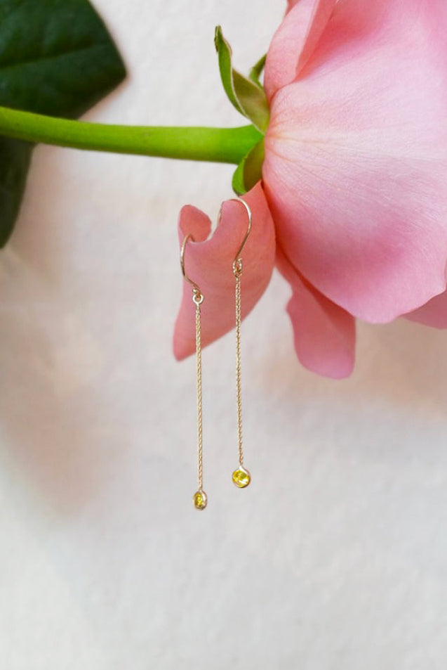 Gold earrings with a yellow citrine gems held against a pink flower and green leaf.