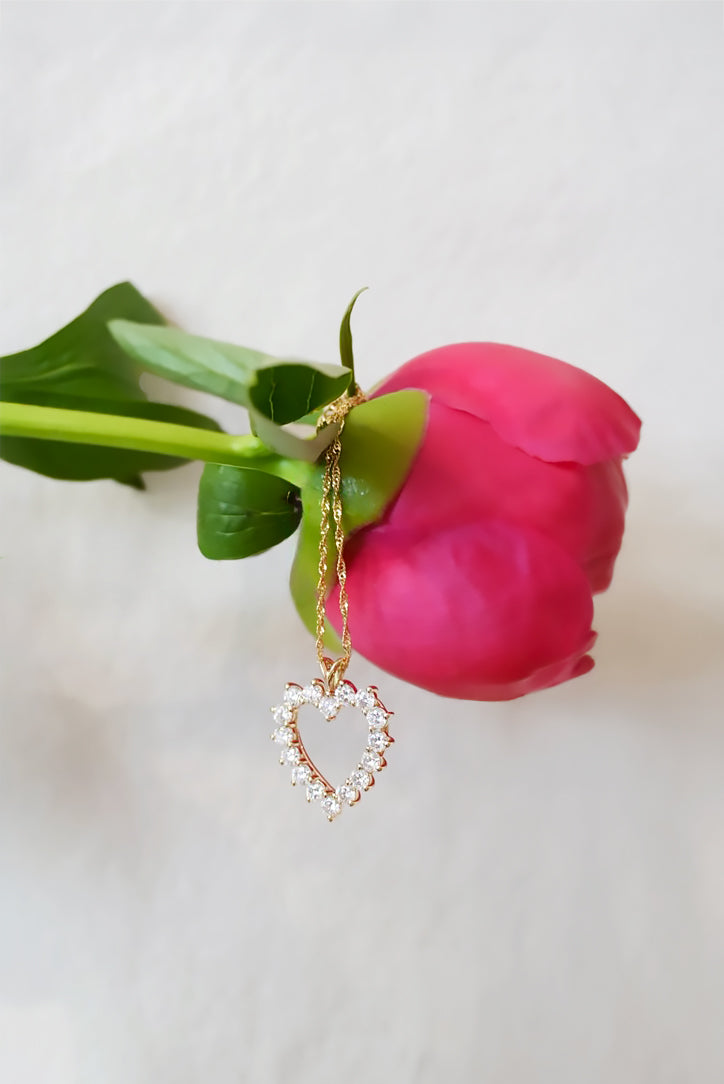 Heart-shaped earring hanging from a pink flower on a light background