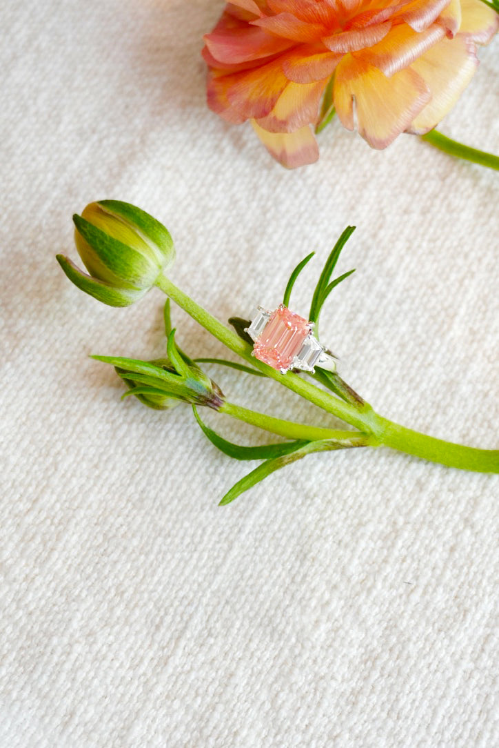 Platinum ring with pink gemstone on a green leafy branch against a light fabric background