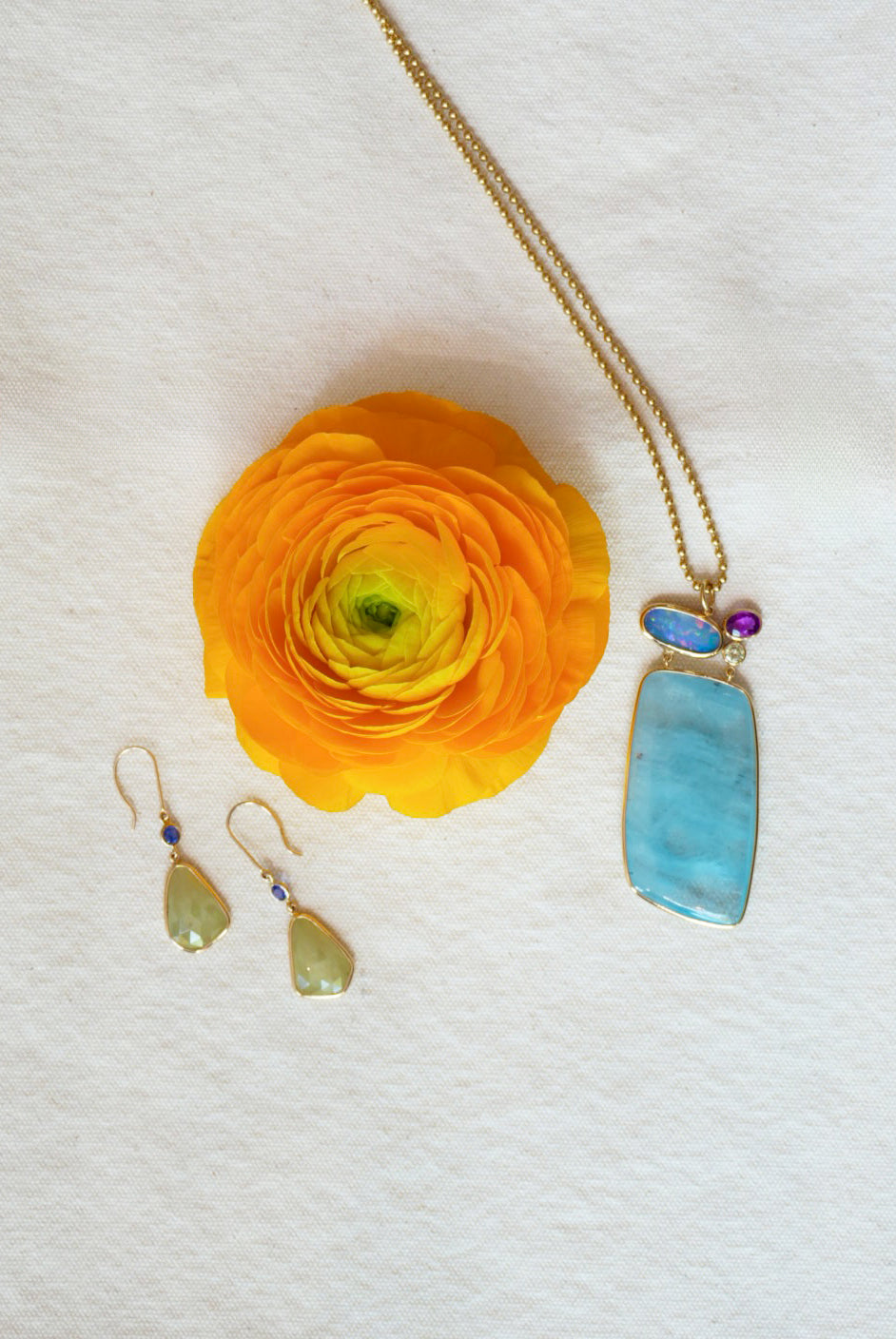 Editorial Jewelry layout with a light blue necklace and green teardrop earrings on a white background with a yellow flower.
