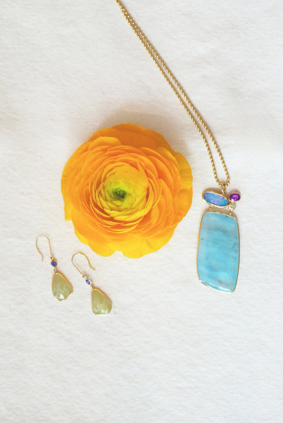 Jewelry set with a light blue pendant and green and purple teardrop earrings on a white background with a yellow flower.