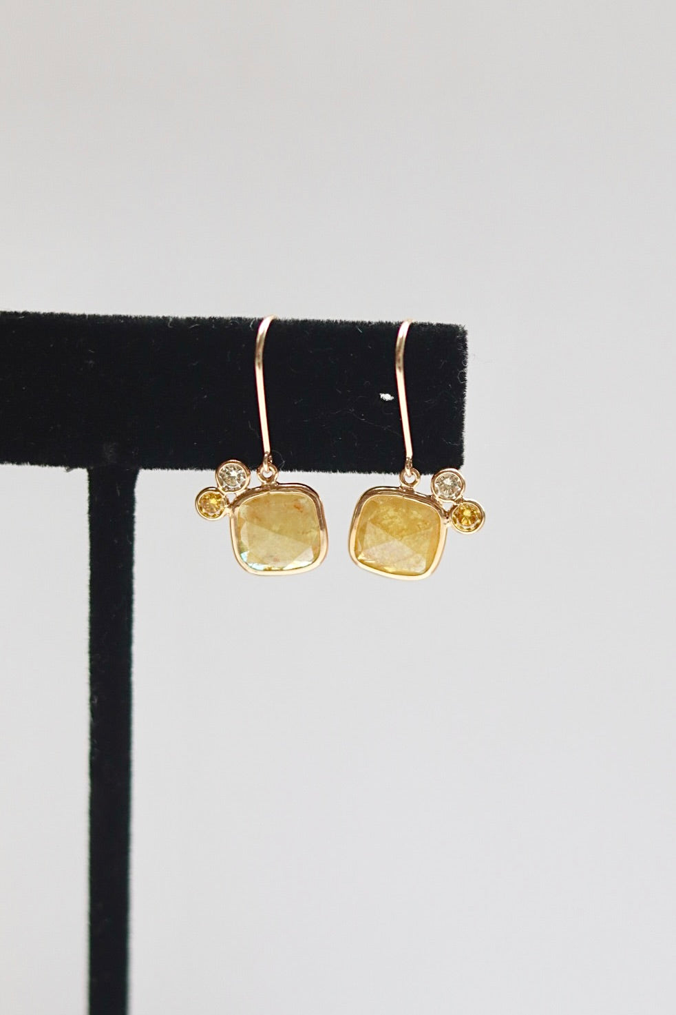 Gold earrings with yellow citrine and diamond gemstones on a black earring stand against a white background