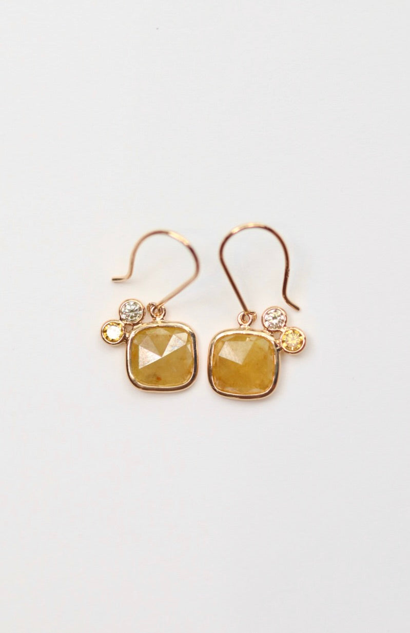 Gold earrings with yellow citrine and diamond gemstones on a light gray background