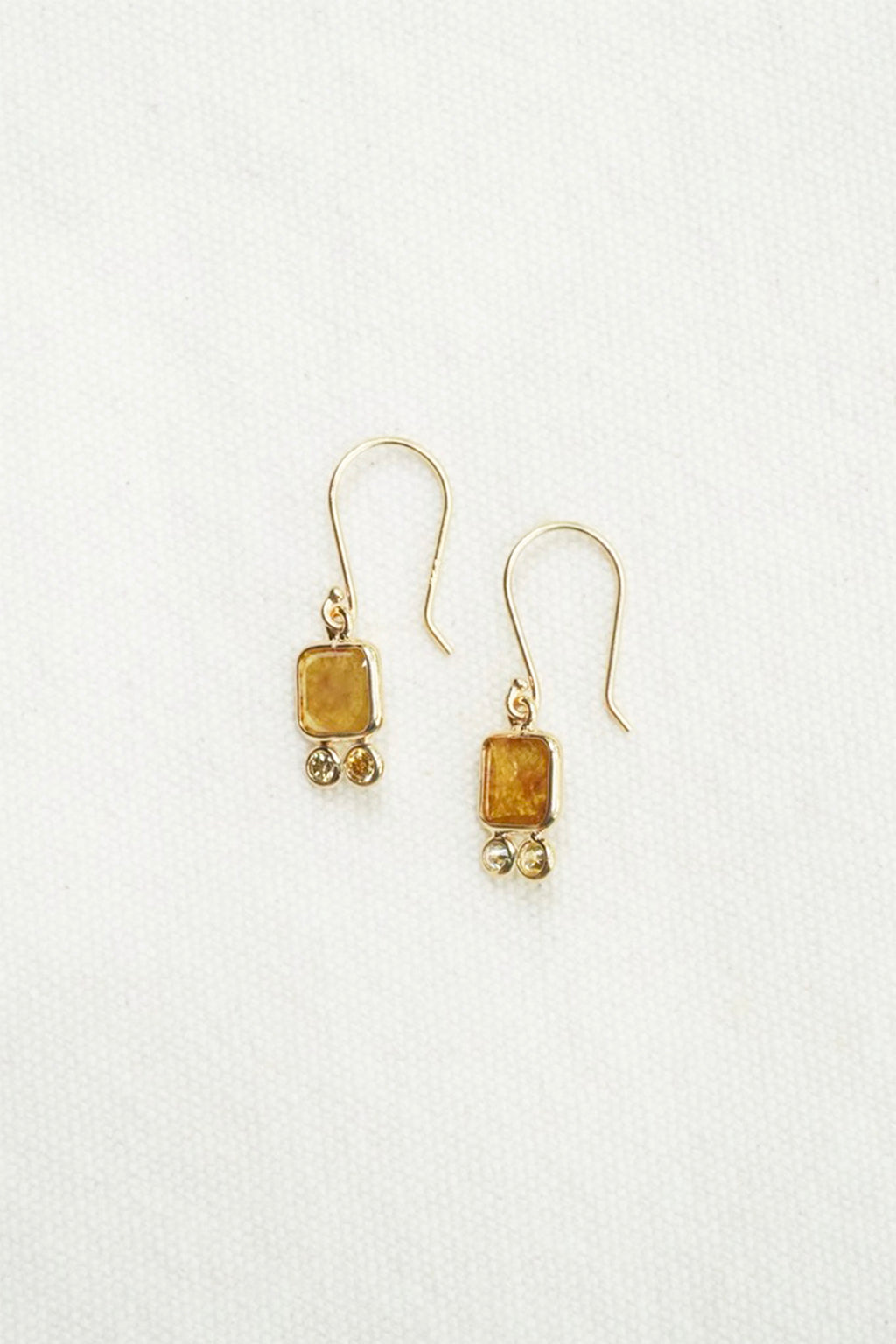 A pair of gold dangle earrings with rectangular amber-yellow stone pendants and small dangling bead accents, shown on a plain white background.