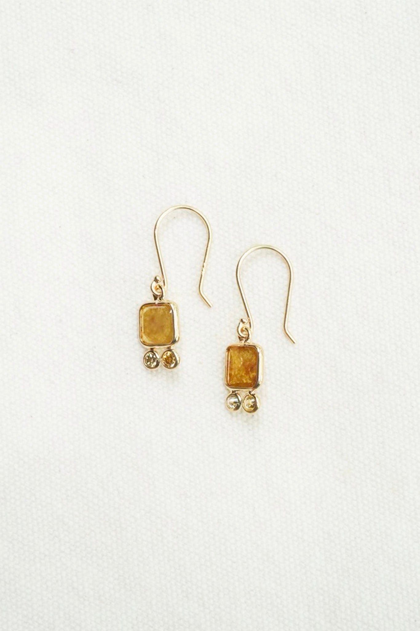 A pair of gold dangle earrings with rectangular amber-yellow stone pendants and small dangling bead accents, shown on a plain white background.