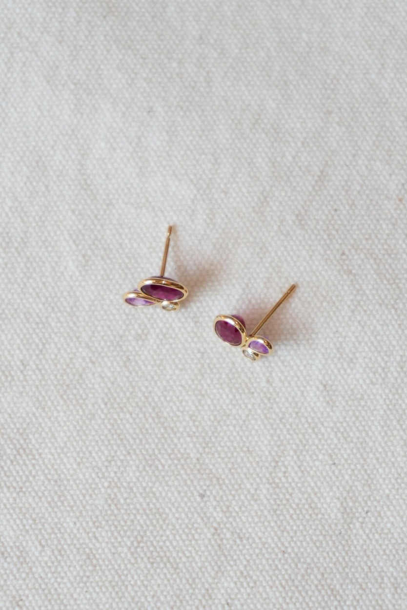 Pair of gold stud earrings with purple stones on a light gray background