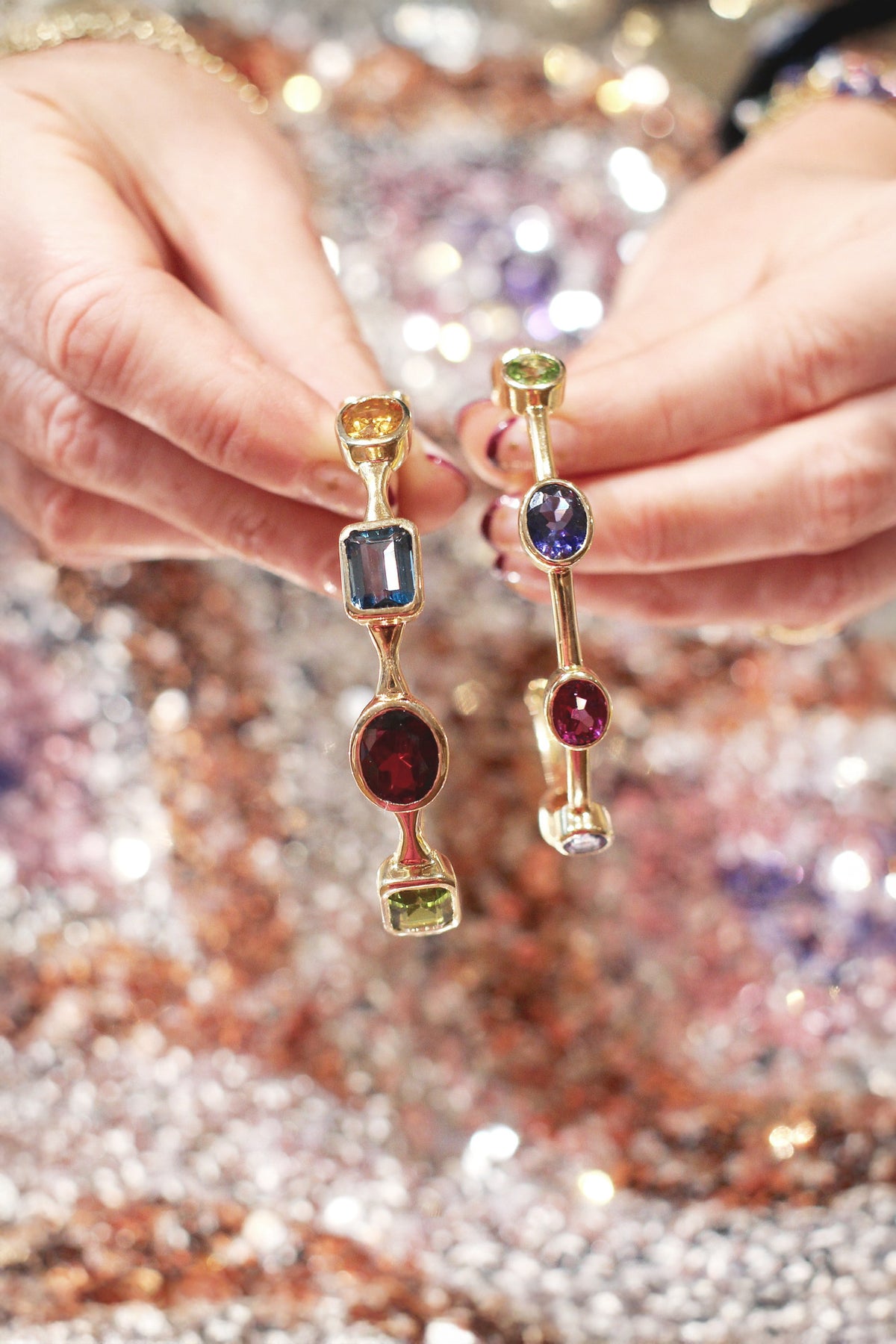Gold bangles with colorful gemstones held by hands against a glittery background