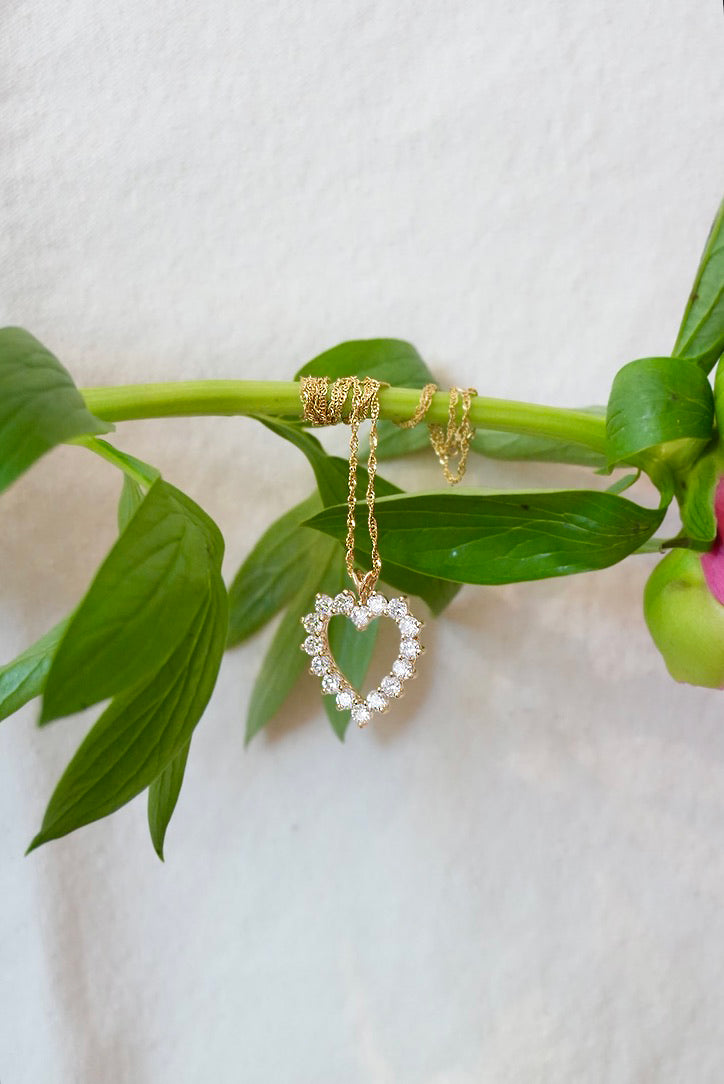 Heart-shaped gold and diamond necklace on a green branch with a white background
