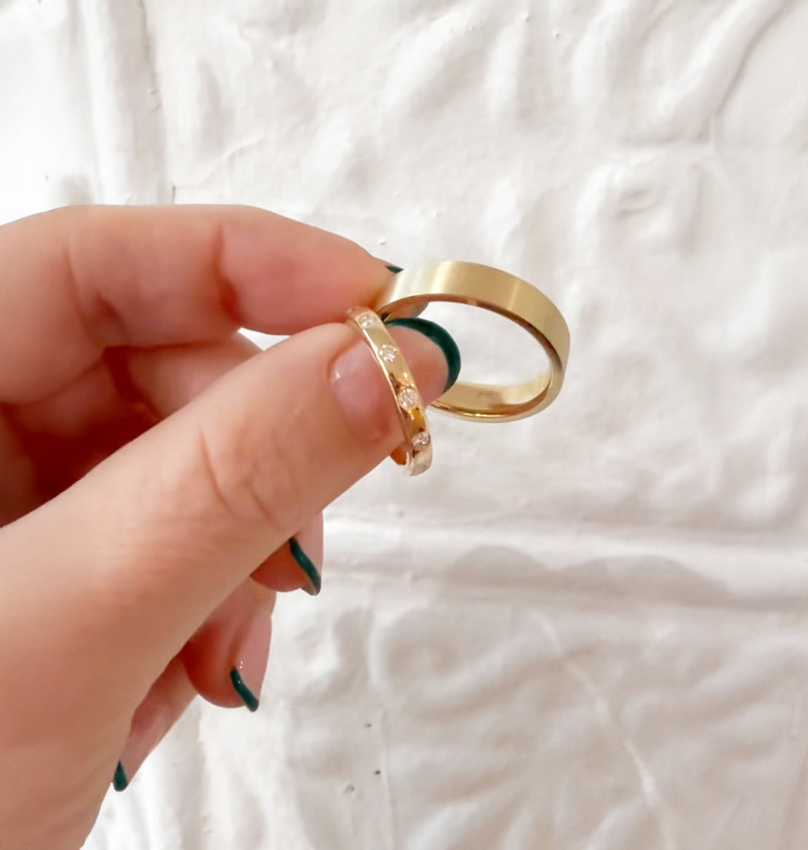 Hand holding two gold rings against a textured white background