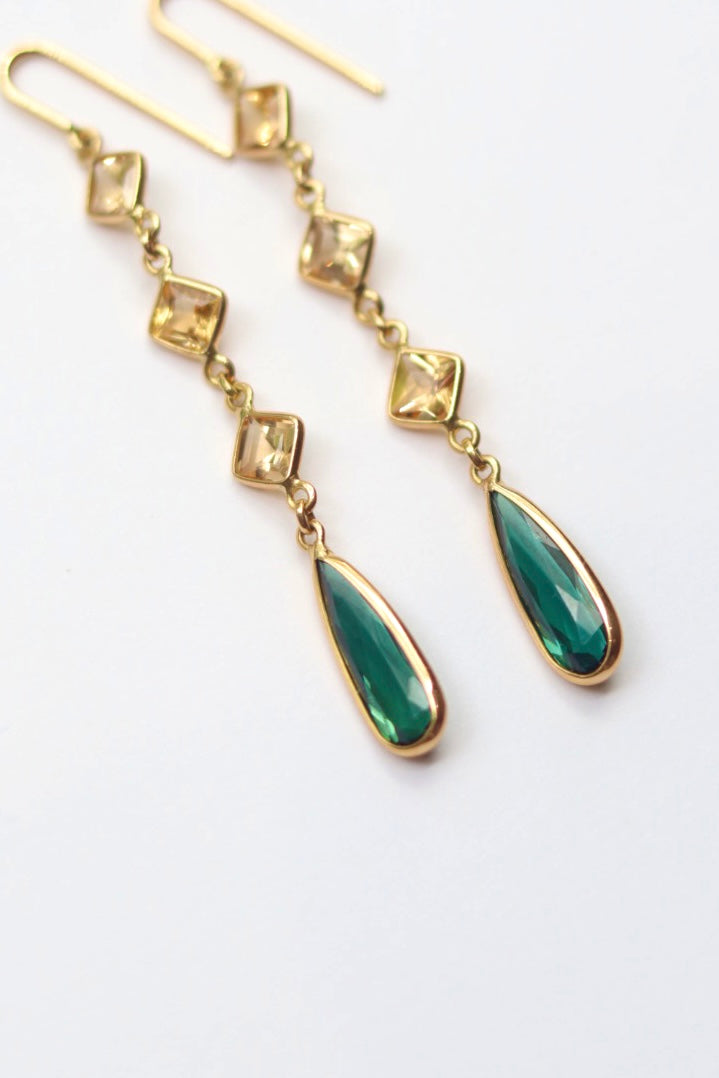 Gold earrings with green teardrop-shaped stones on a white background