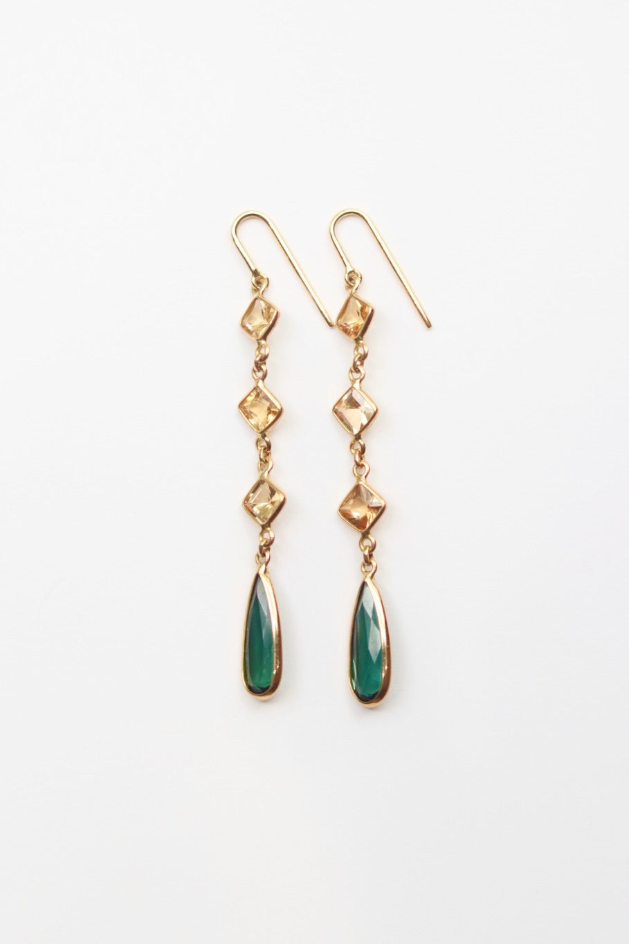 Gold earrings with green teardrop-shaped stones on a white background