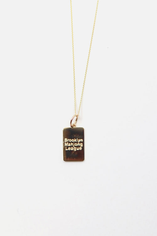 Gold mahjong necklace with a rectangular pendant on a white background