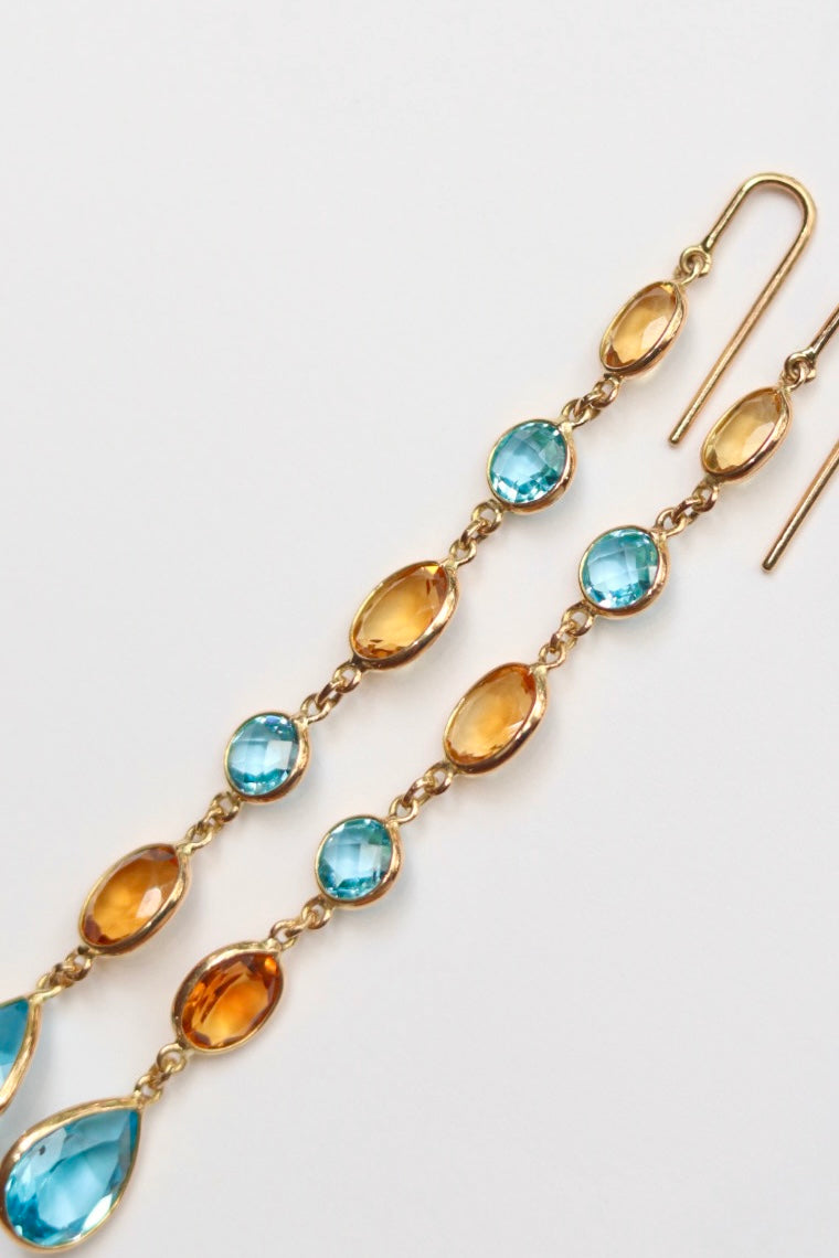 Gold earrings with blue and amber gemstones on a light gray background
