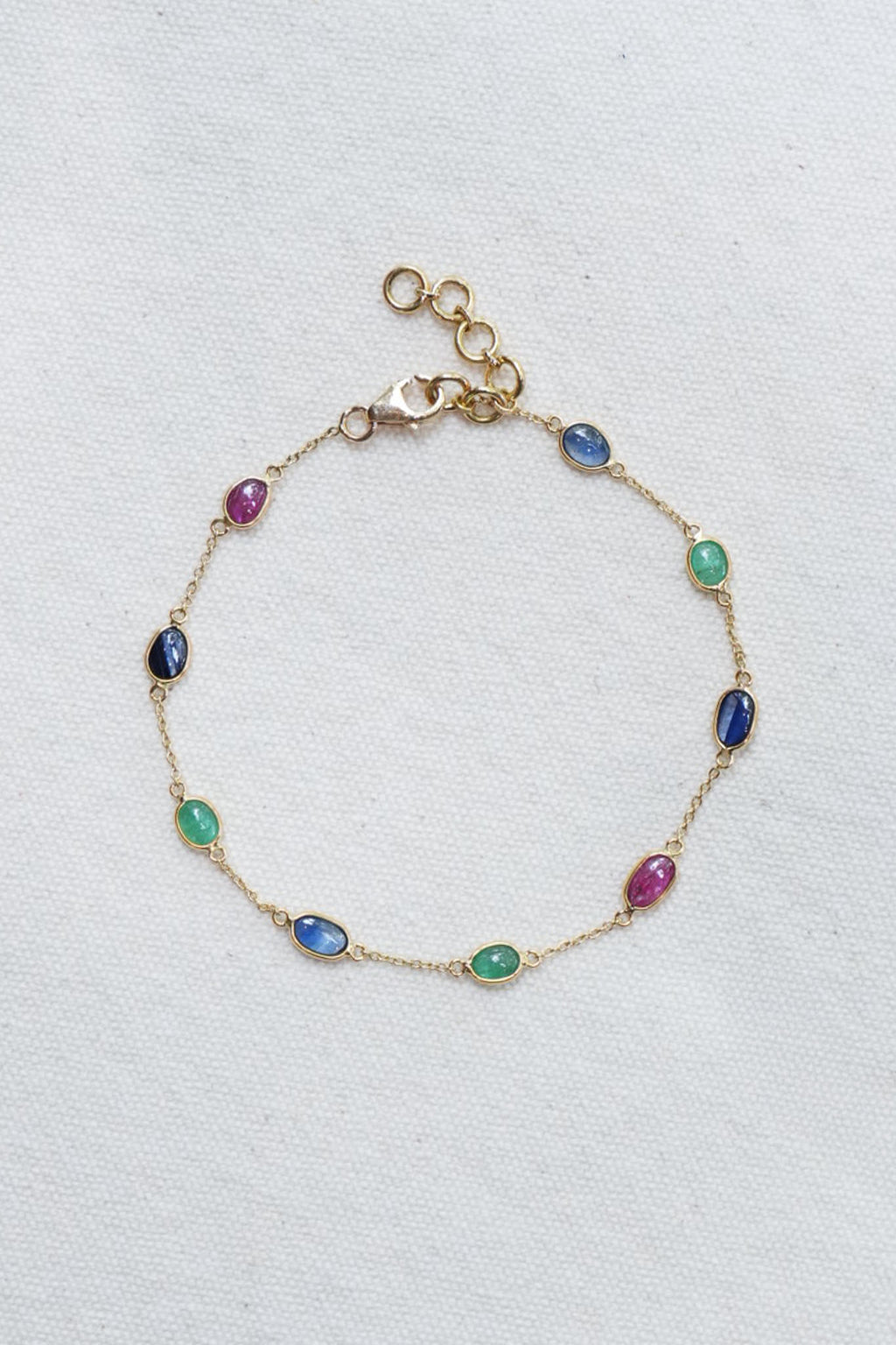Gold bracelet with multicolored gemstones on a light gray background