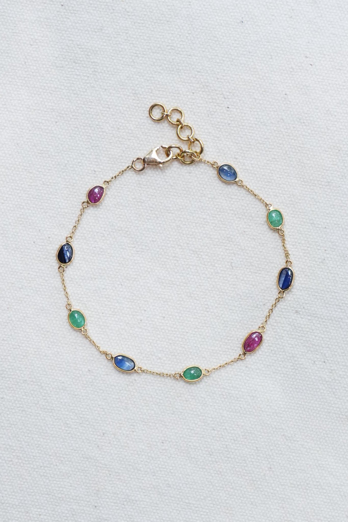 Gold bracelet with multicolored gemstones on a light gray background