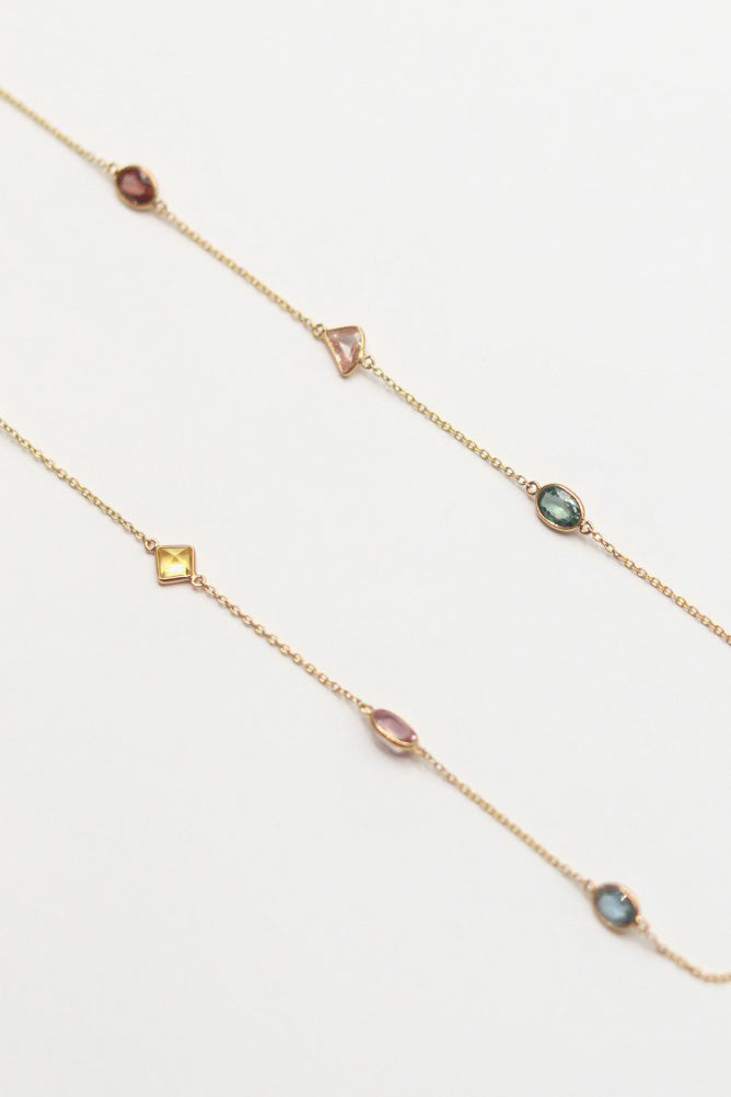 Delicate gold necklace with small colorful gemstones on a light gray background