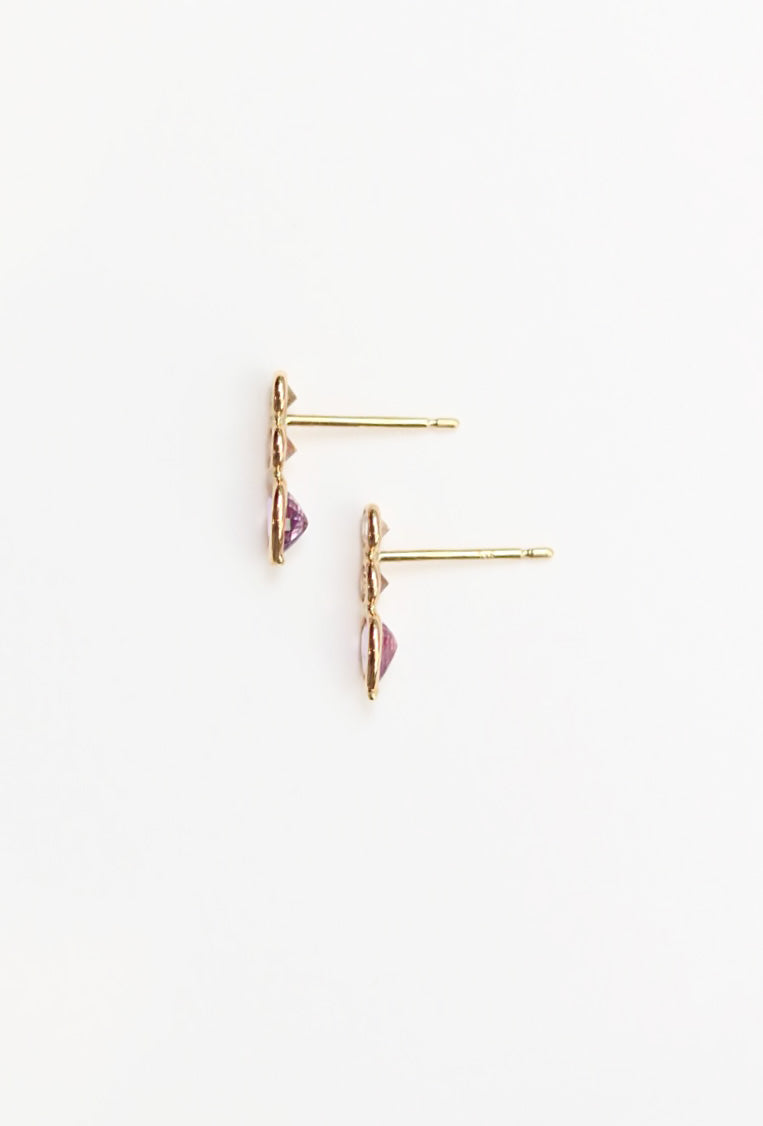 Gold earrings on their side with pink gemstones on a white background