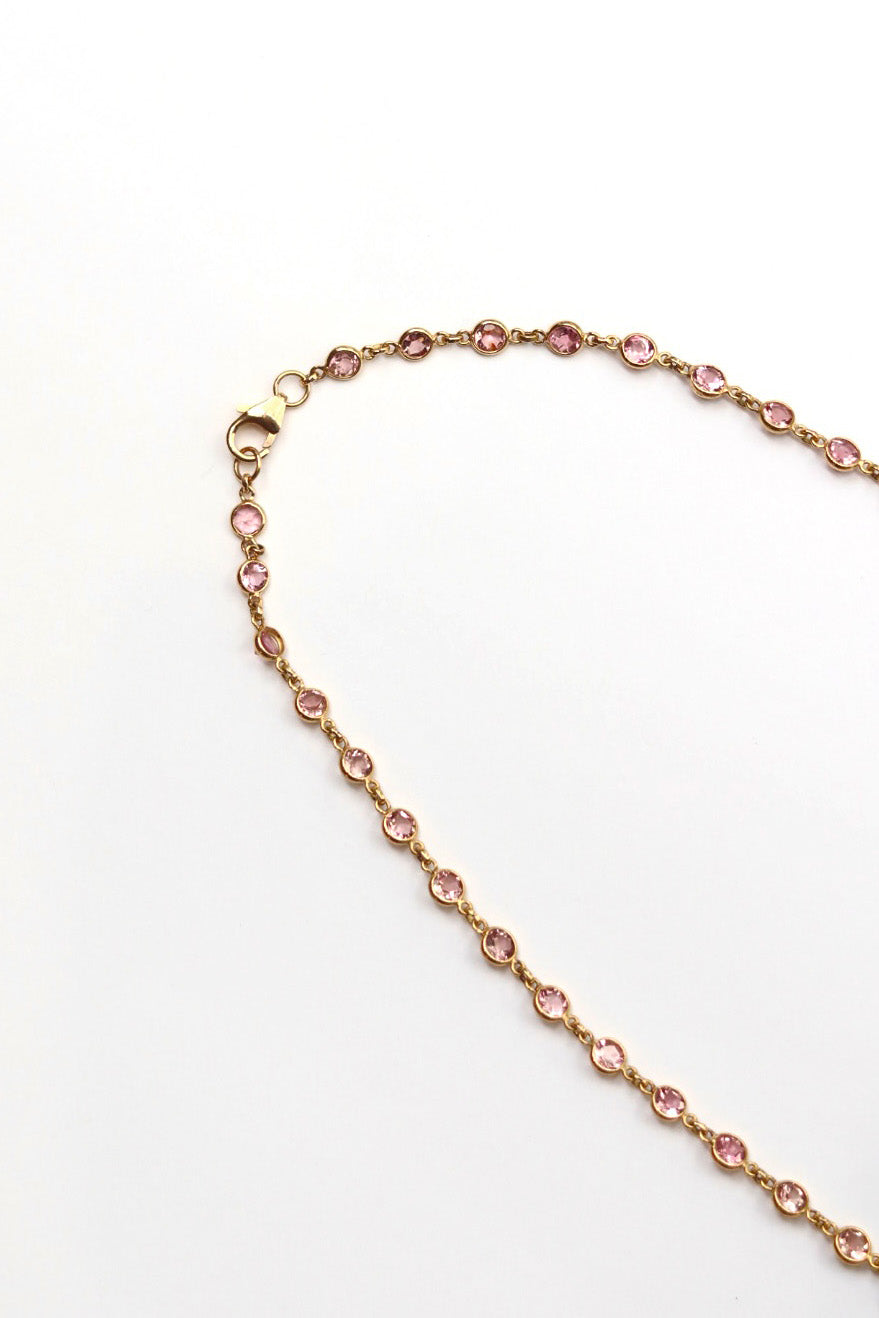 Gold necklace with pink gemstones on a white background