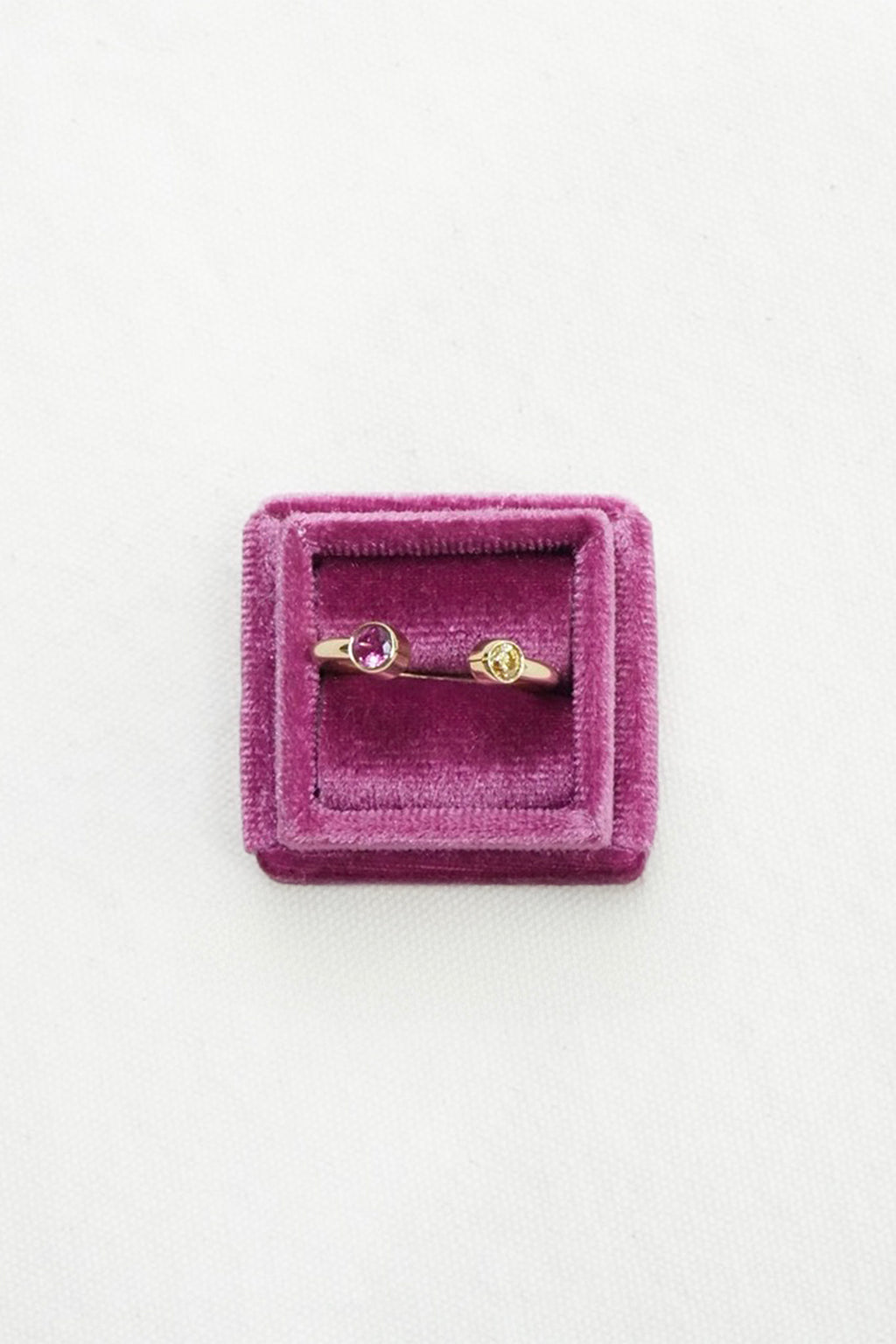 Gold ring with small pink gemstones displayed on a square purple velvet ring box against a white background.