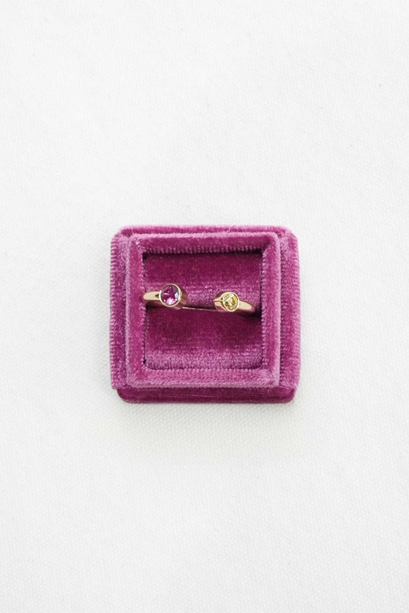 Gold ring with small pink gemstones displayed on a square purple velvet ring box against a white background.