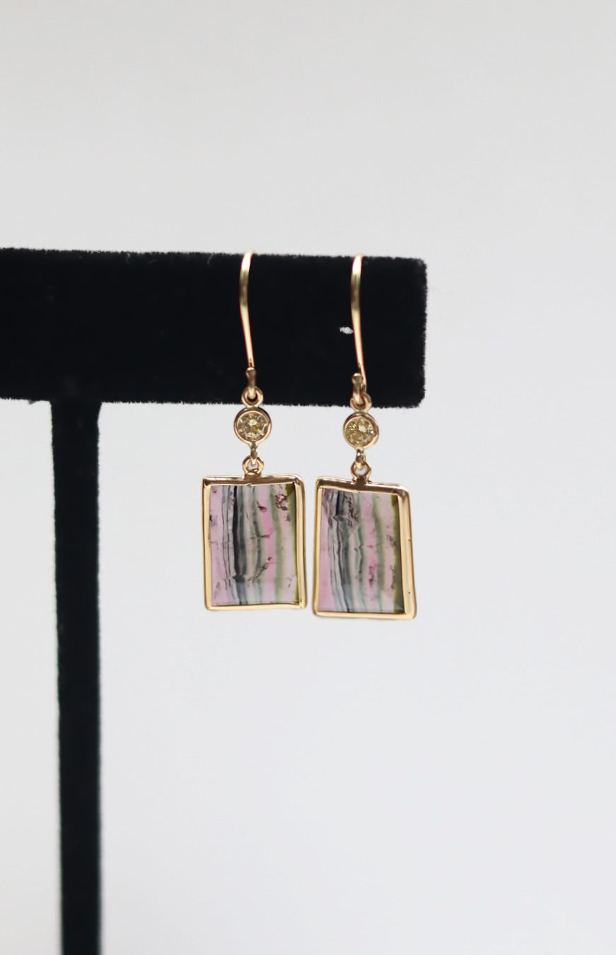 Gold-framed rectangular stone earrings on a black earring stand with a white background