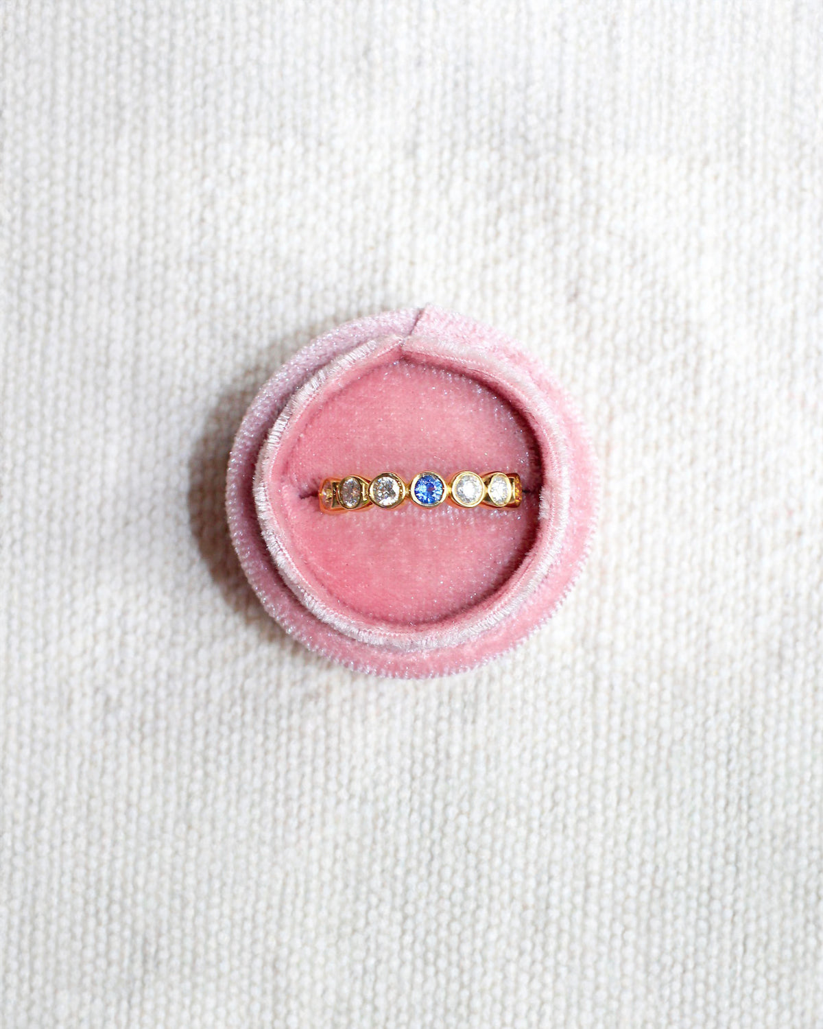 Ring with colorful gemstones in a pink velvet box on a white background