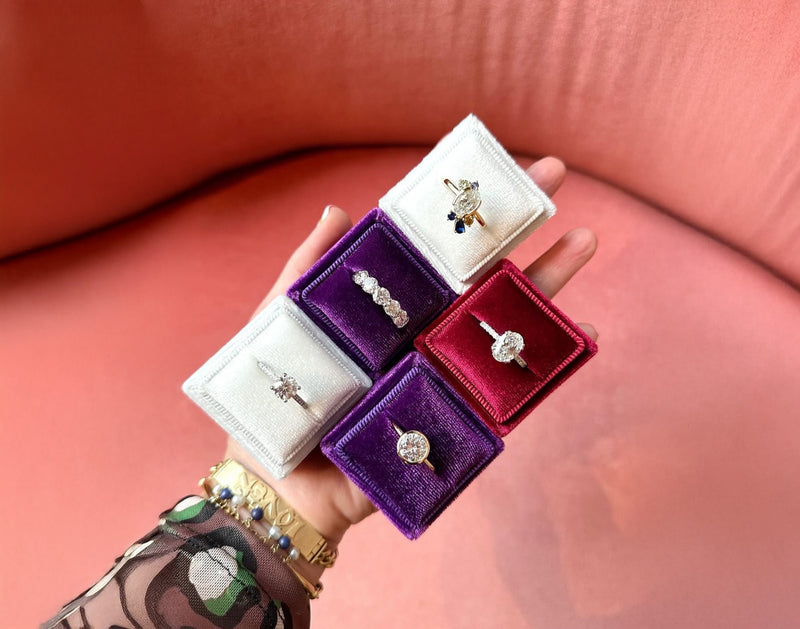 Hand holding a small jewelry box with rings on a pink surface