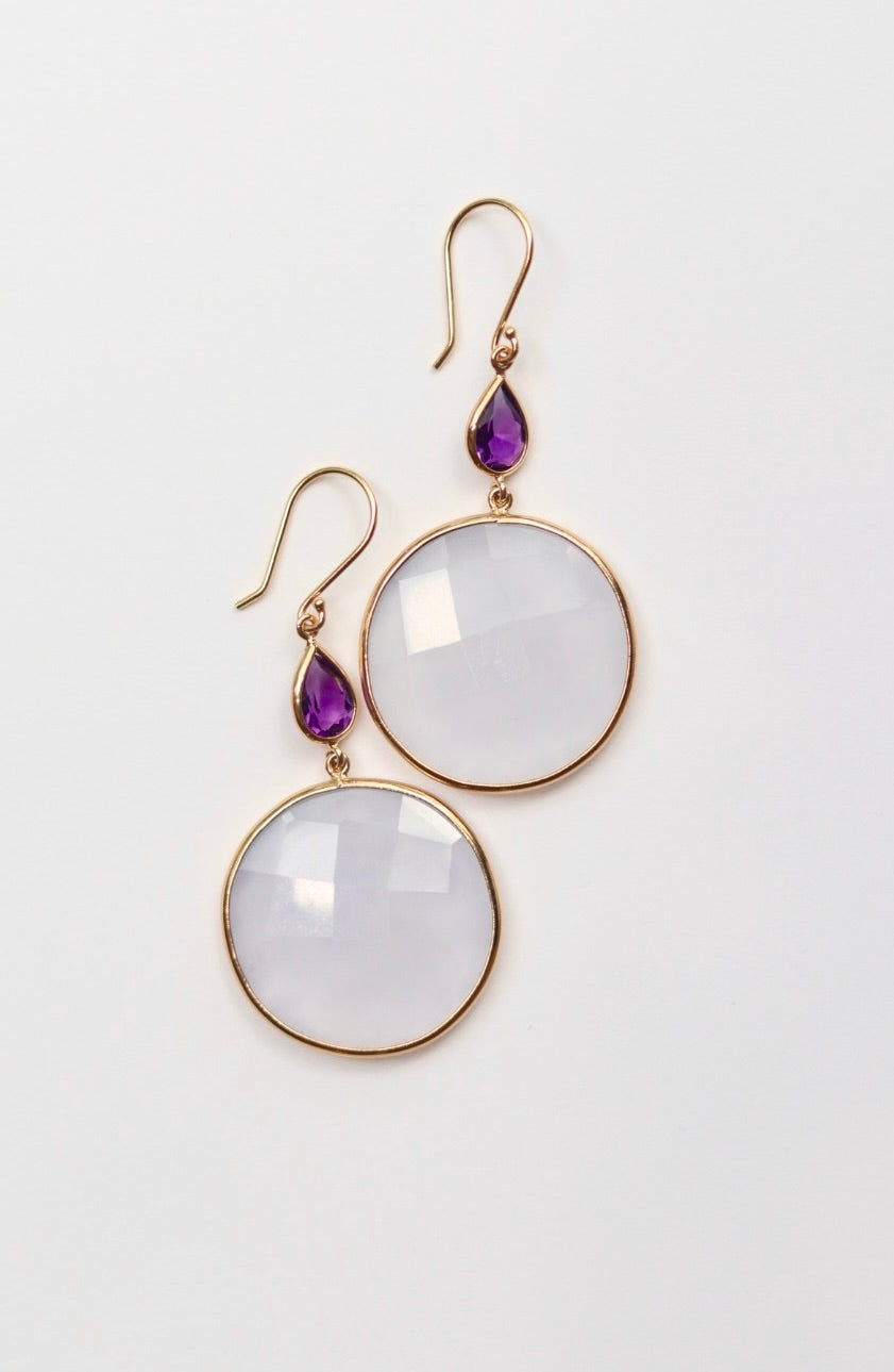 Pair of earrings with round white stones and purple teardrop stones on a light gray background