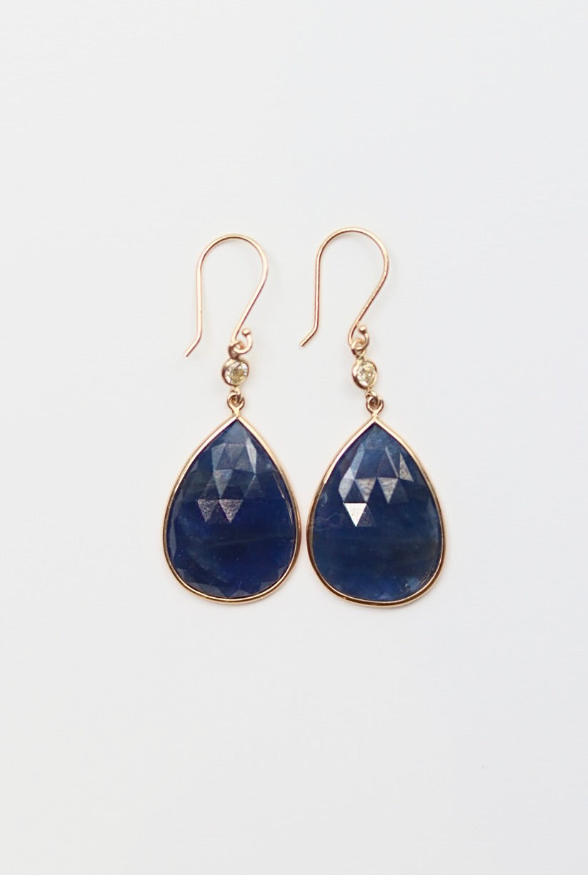 Teardrop-shaped blue gemstone earrings with gold accents on a light gray background