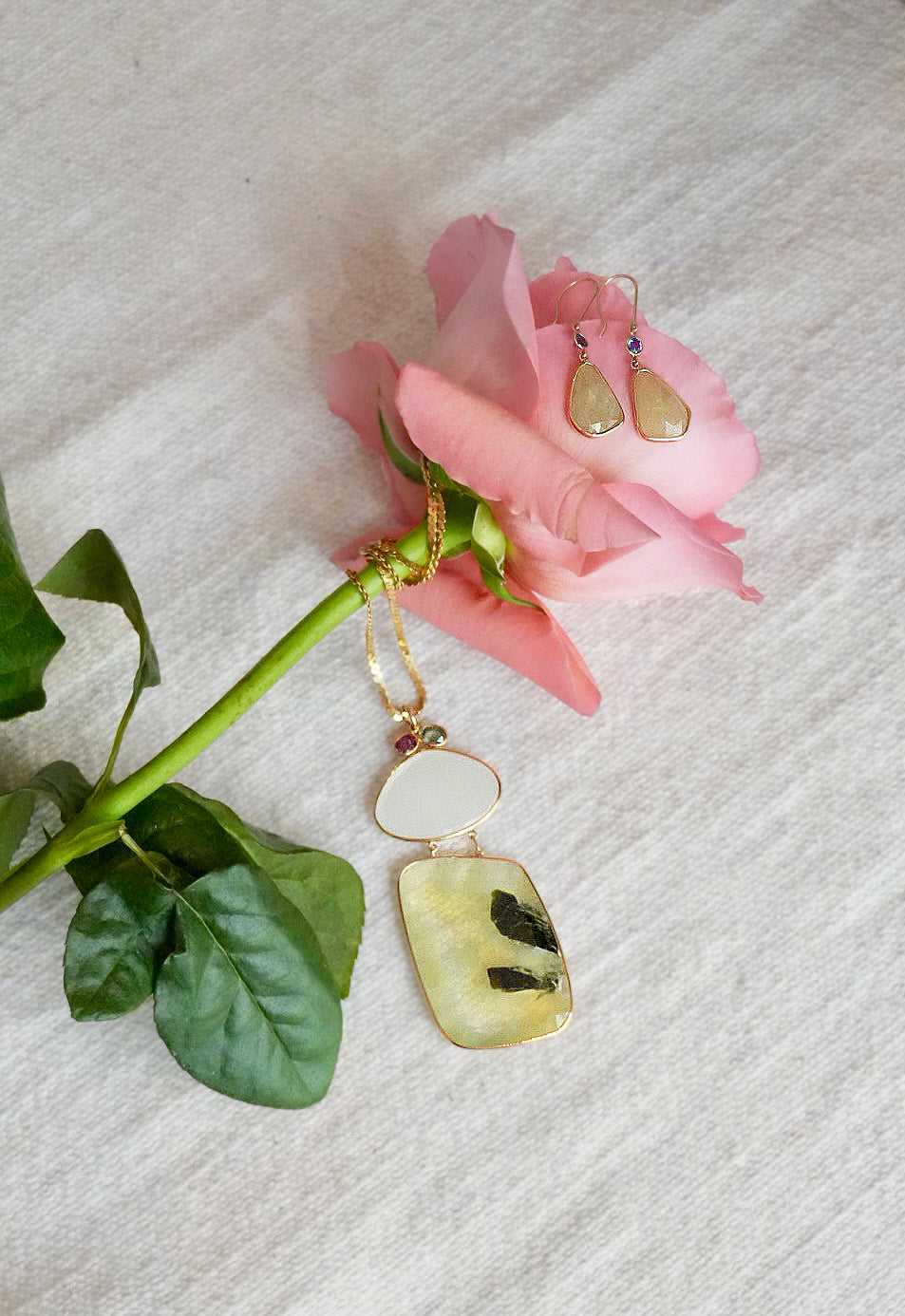 Pair of earrings and statement necklace with a pink rose on a textured white surface
