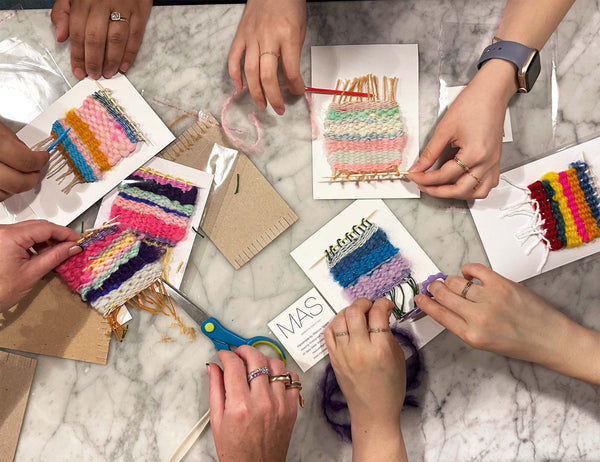 People working on colorful woven crafts on a marble surface