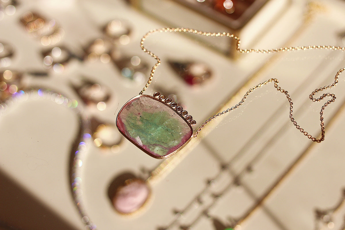 Necklace with a pink and green stone pendant on a reflective surface