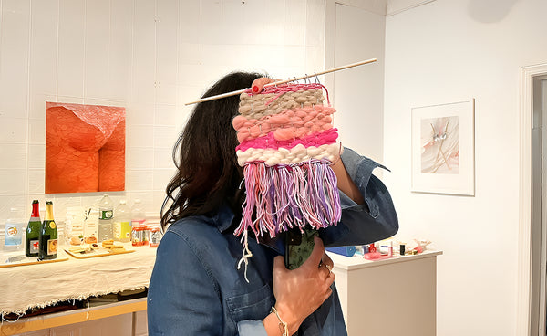Person holding a colorful woven wall hanging in a room with art on the wall