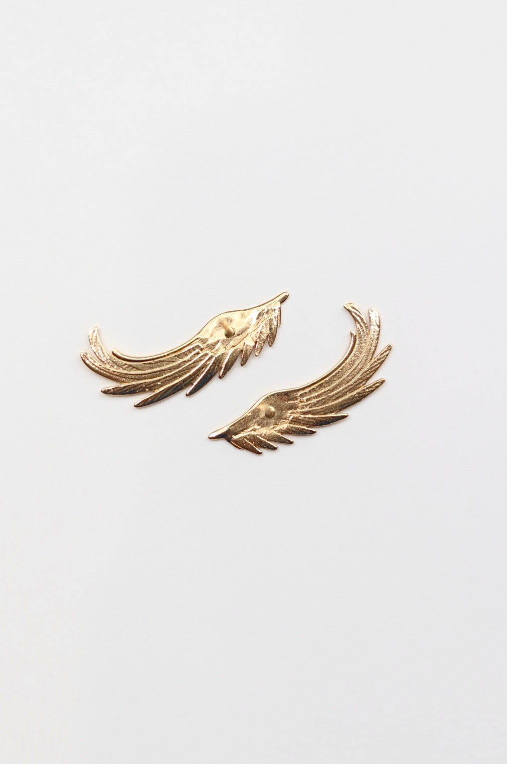 Gold wing-shaped earrings on a light gray background