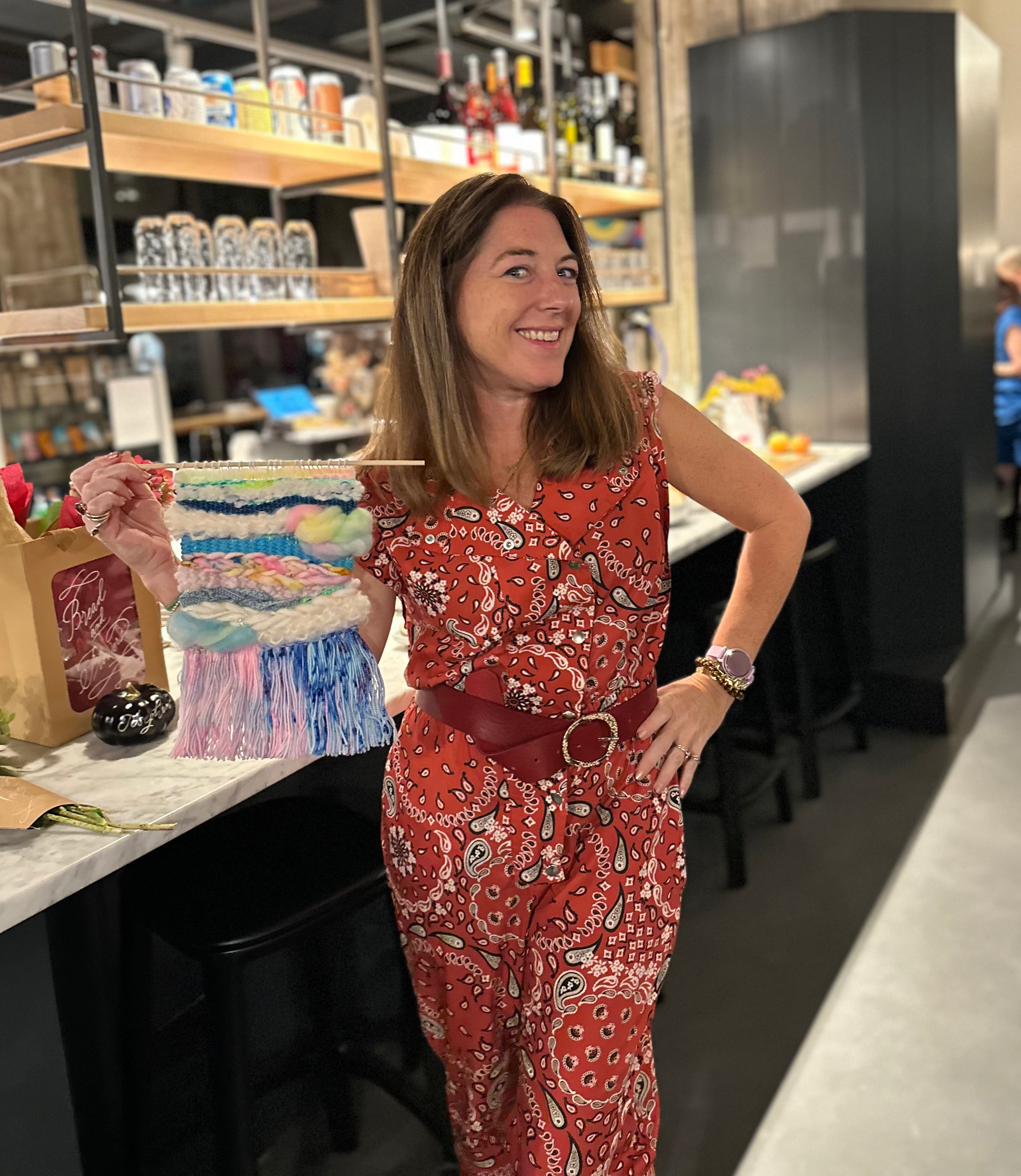 Woman in a red patterned outfit holding a colorful cake-shaped object in a store setting.