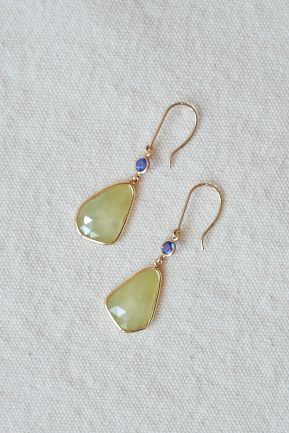 Pair of earrings with green teardrop-shaped stones on a light gray fabric background