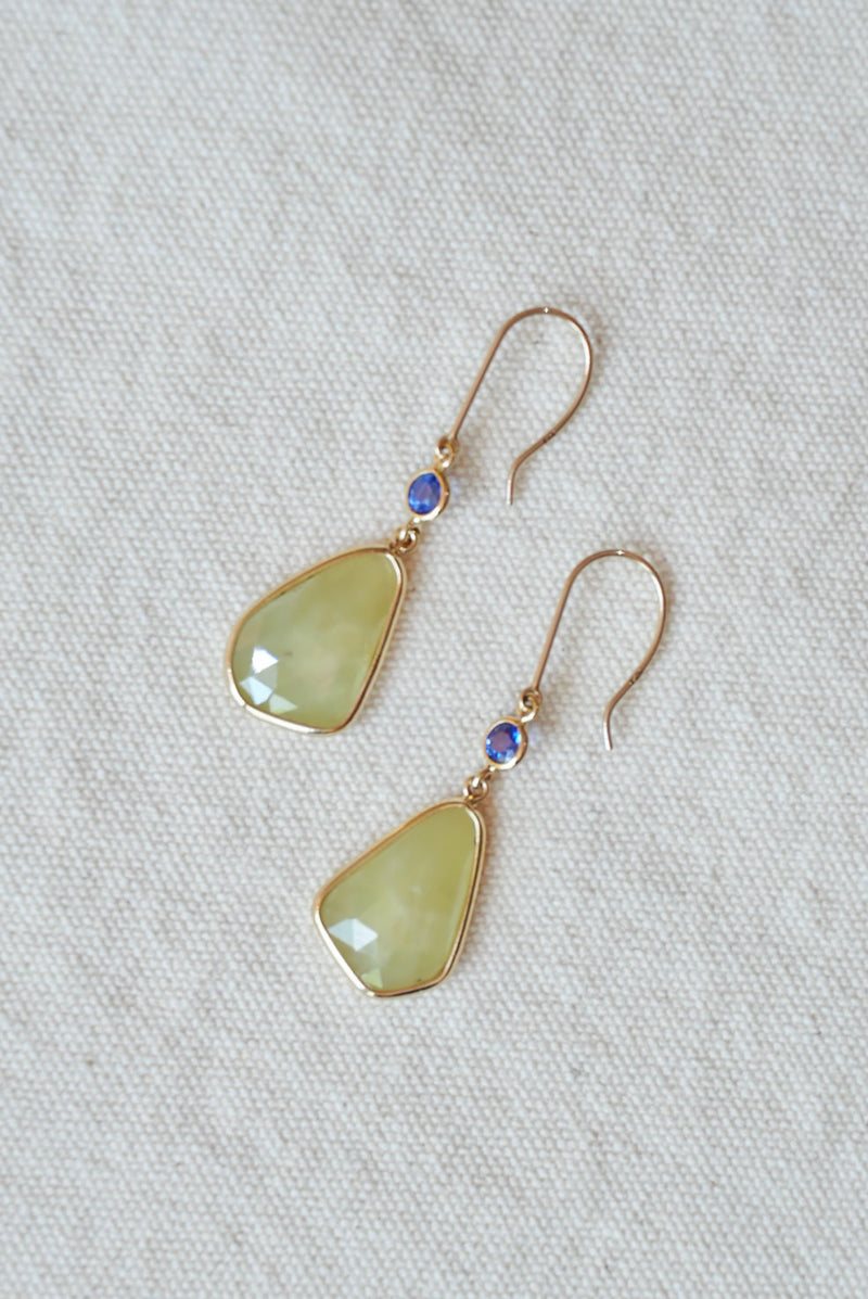 Pair of earrings with green teardrop-shaped stones on a light gray fabric background