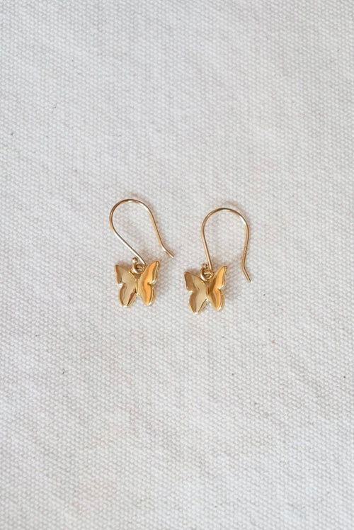 Gold butterfly-shaped earrings on a light cream fabric background