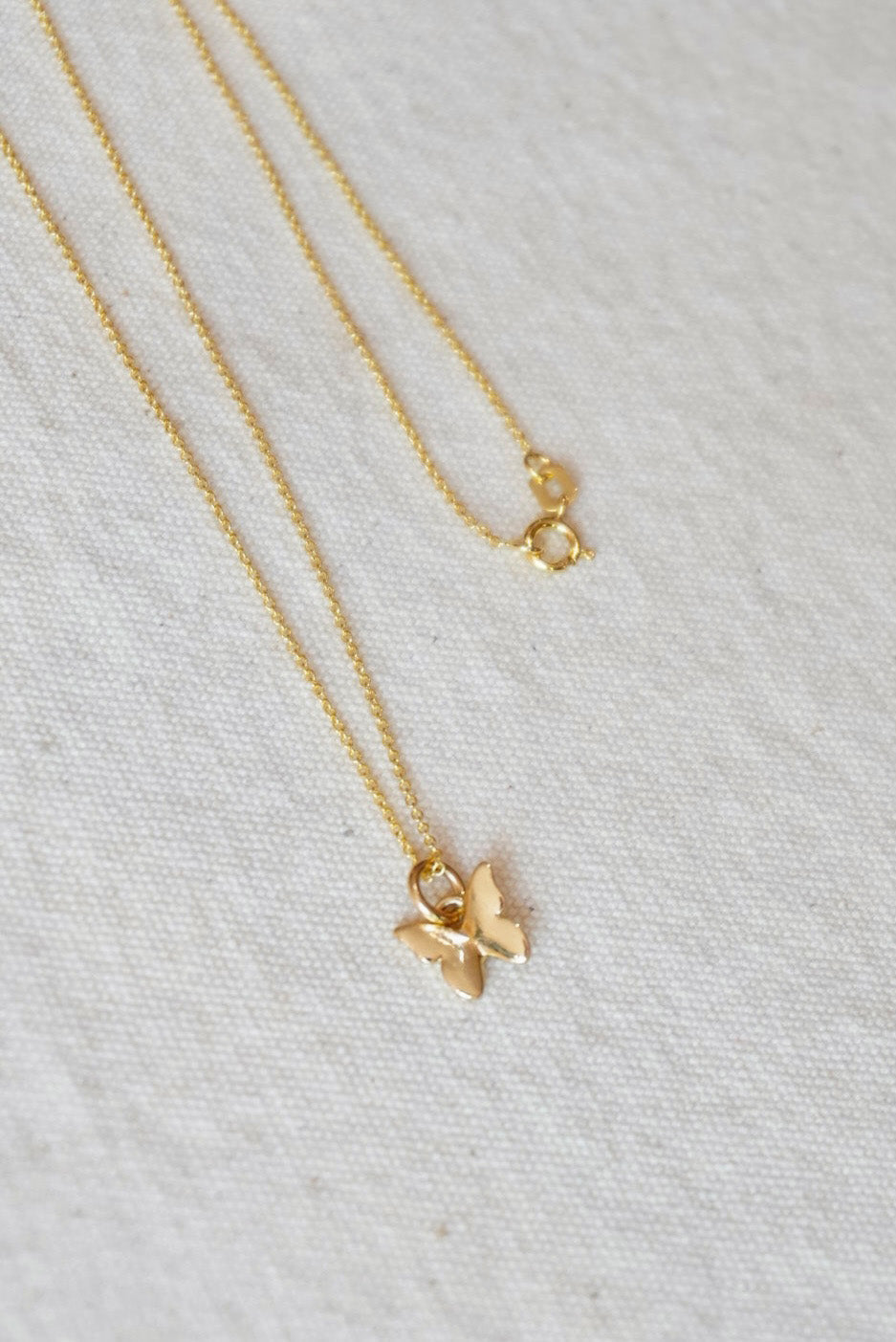 Gold necklace with a small butterfly pendant on a light gray fabric background