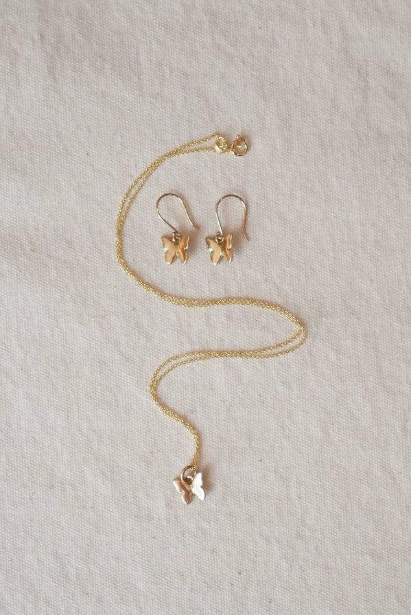 Gold butterfly necklace and earrings on a beige fabric background