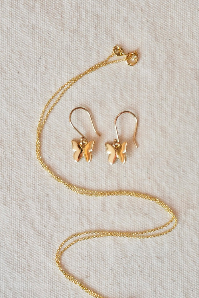 Gold butterfly necklace and earrings on a cream fabric background
