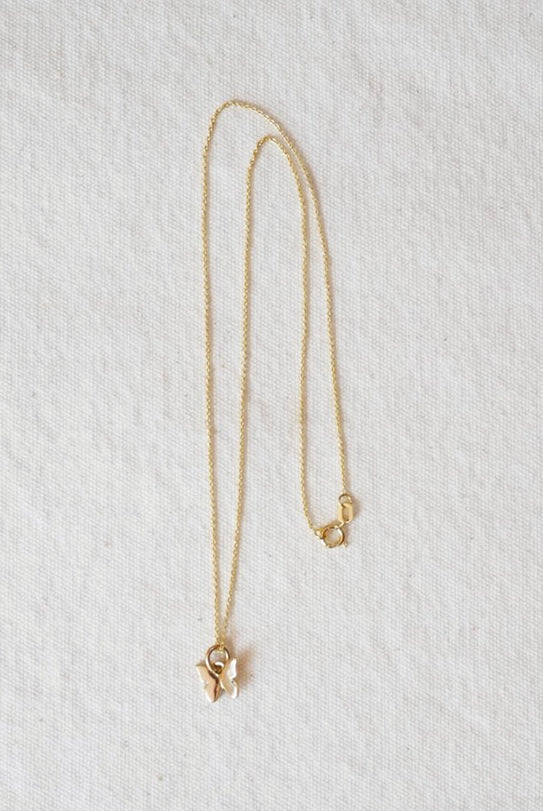 Gold necklace with a small butterfly pendant on a light gray textured background