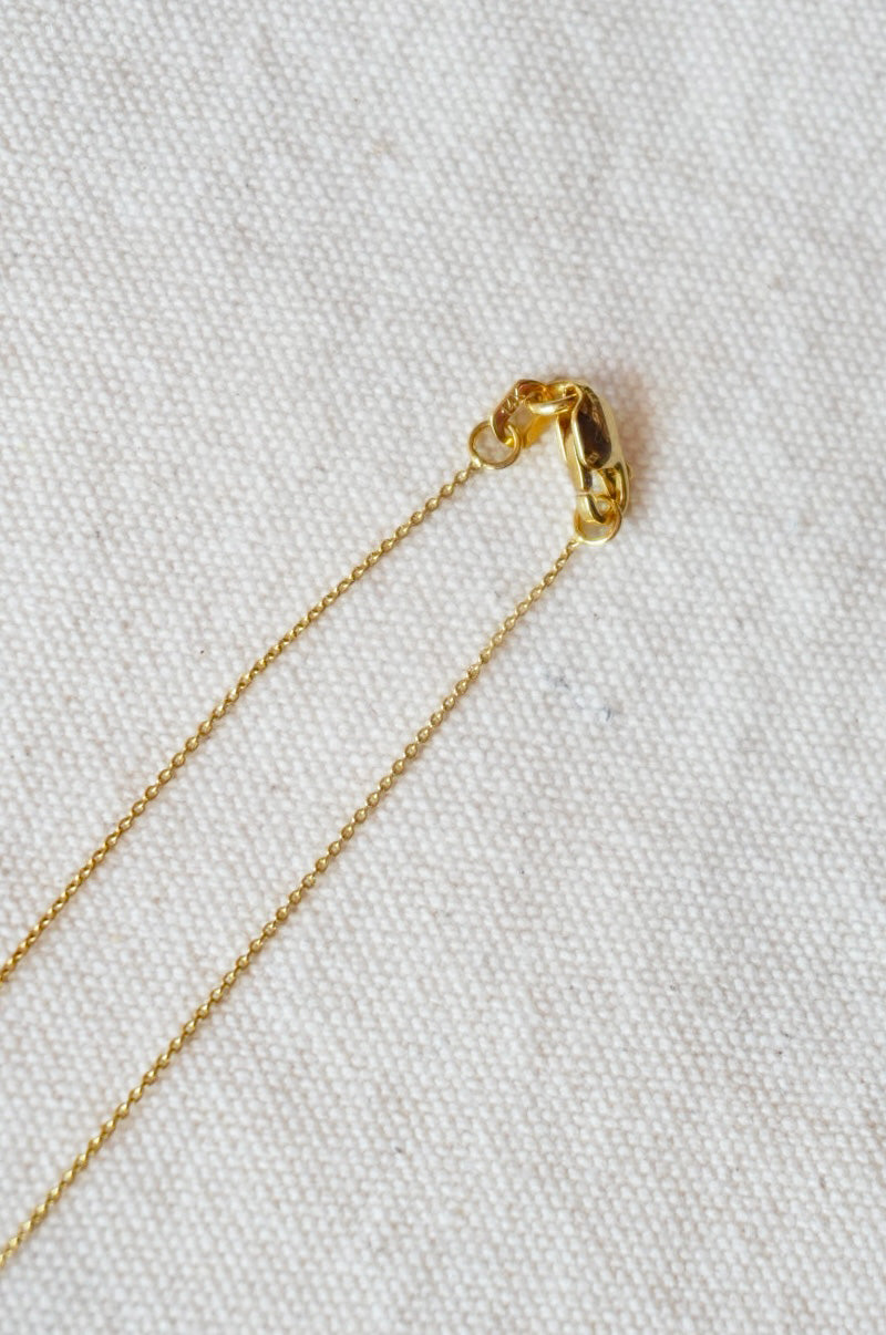 Gold chain necklace on a textured beige fabric background