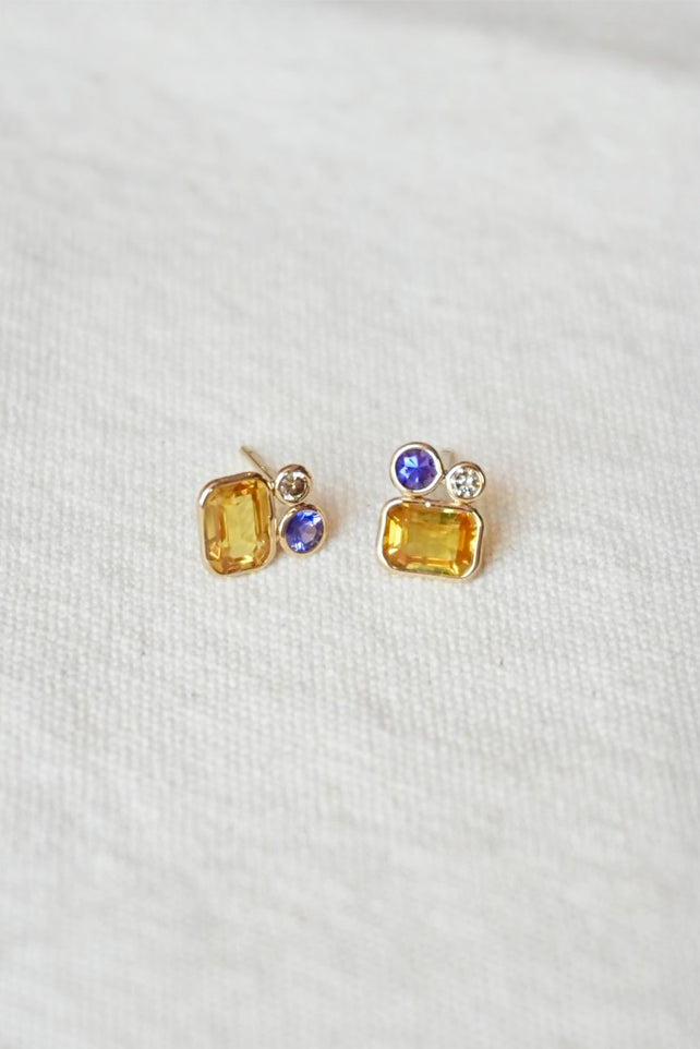 Pair of gold stud earrings with yellow and purple gemstones on a white background