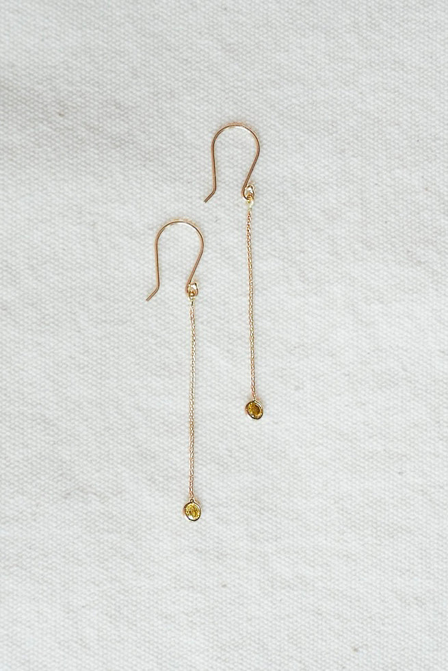 Gold earrings with small round citrine stones on a light gray textured background