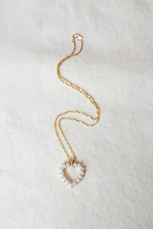 Gold necklace with a heart-shaped pendant on a light background